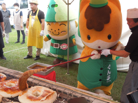 写真2：焼きまんじゅうに味噌を塗るぐんまちゃん、後ろで見守るぬまたんち