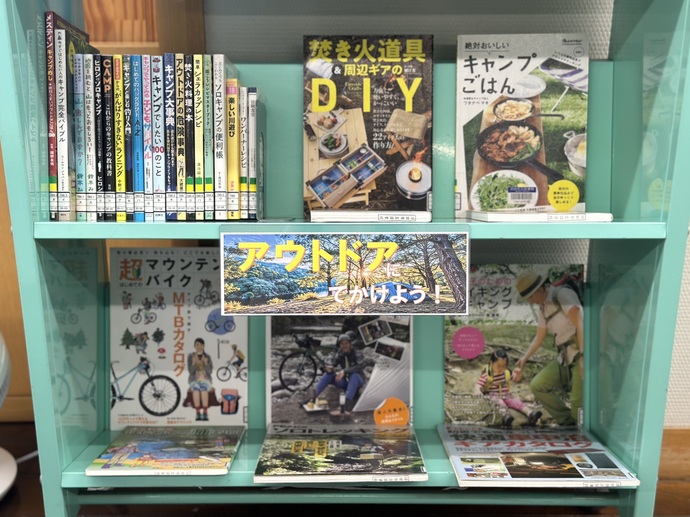 アウトドア特集として、キャンプや焚き火などに関する本がブックトラックの上に並べられている。